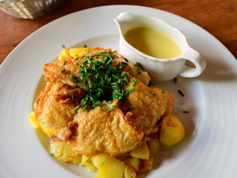 Pannfisch mit Bratkartoffeln und Senfsoße auf einem weißen Teller.