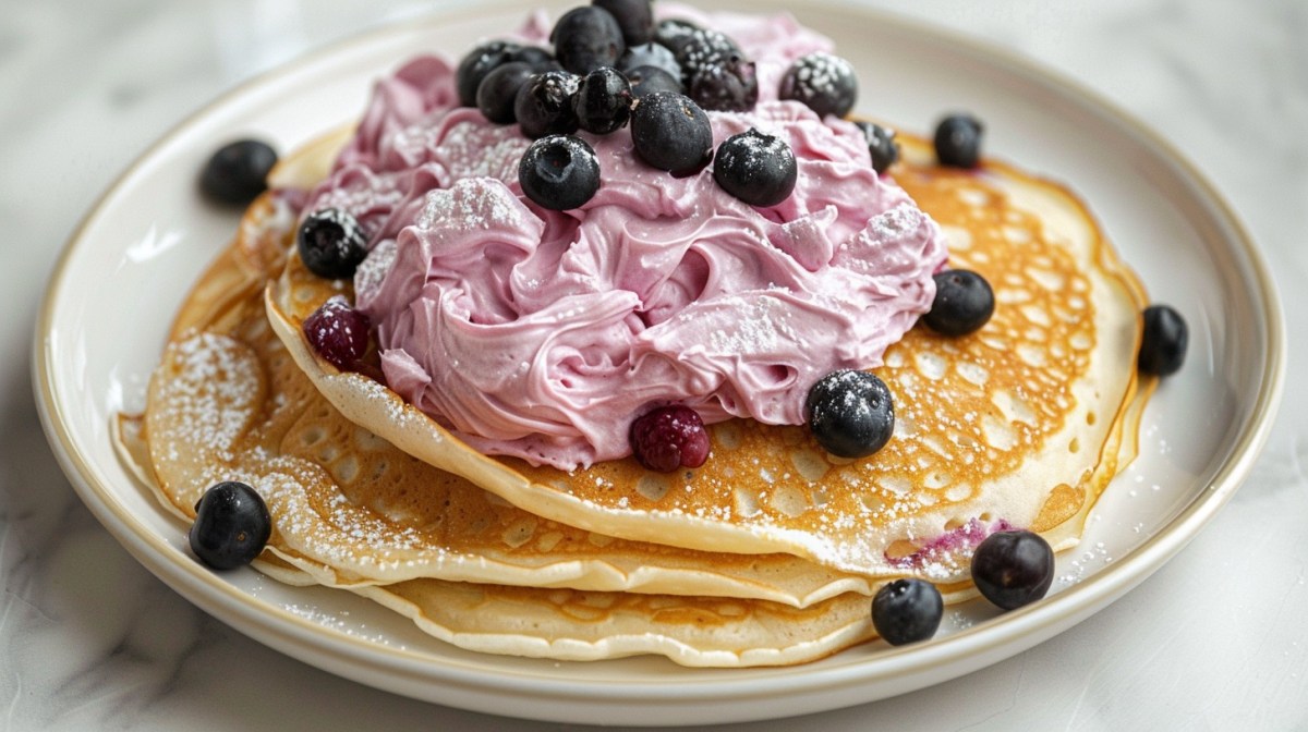 ein paar Pfannkuchen mit Blaubeercreme auf einem Teller, garniert mit frischen Blaubeeren und Puderzucker.