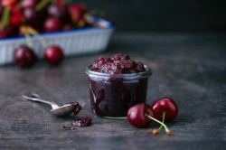 Ein Glas mit Schwarzwälder Kirschmarmelade und Kirschen auf dem Tisch