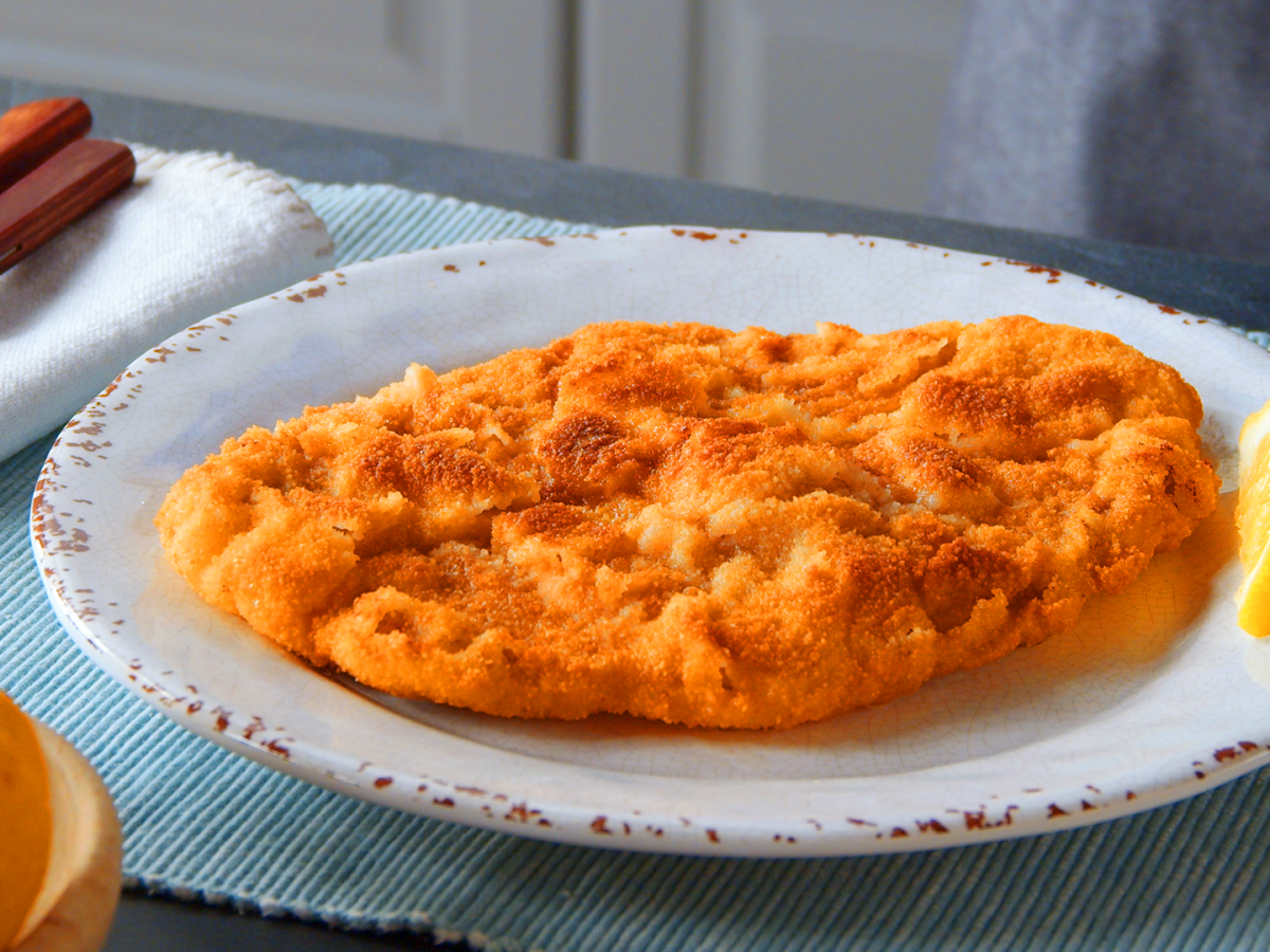 Schweineschnitzel auf einem weißen Teller. Daneben liegt eine Zitronenspalte.