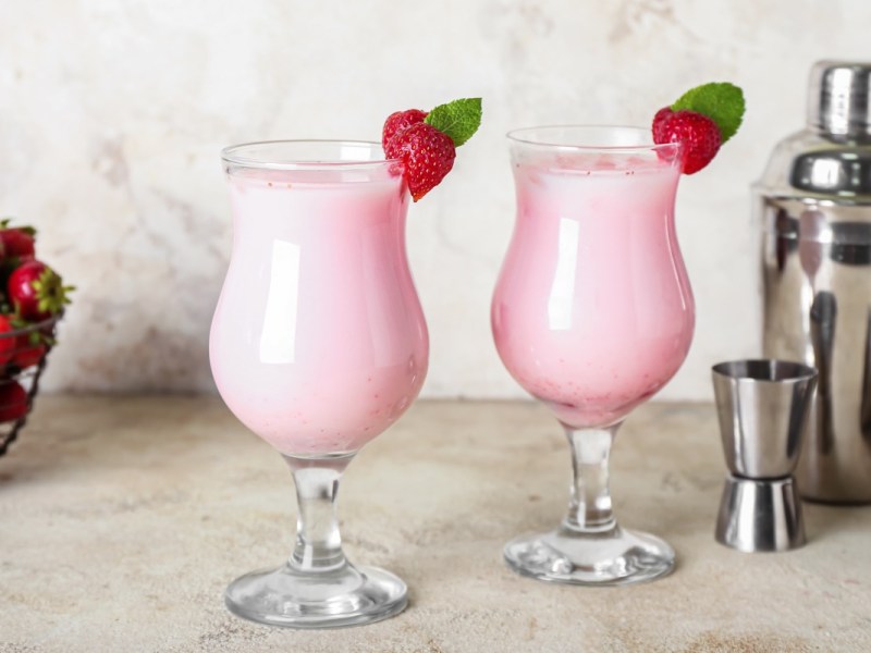 Zwei Gläser Strawberry Colada mit Erdbeeren als Deko. Daneben stehen Cocktailshaker.