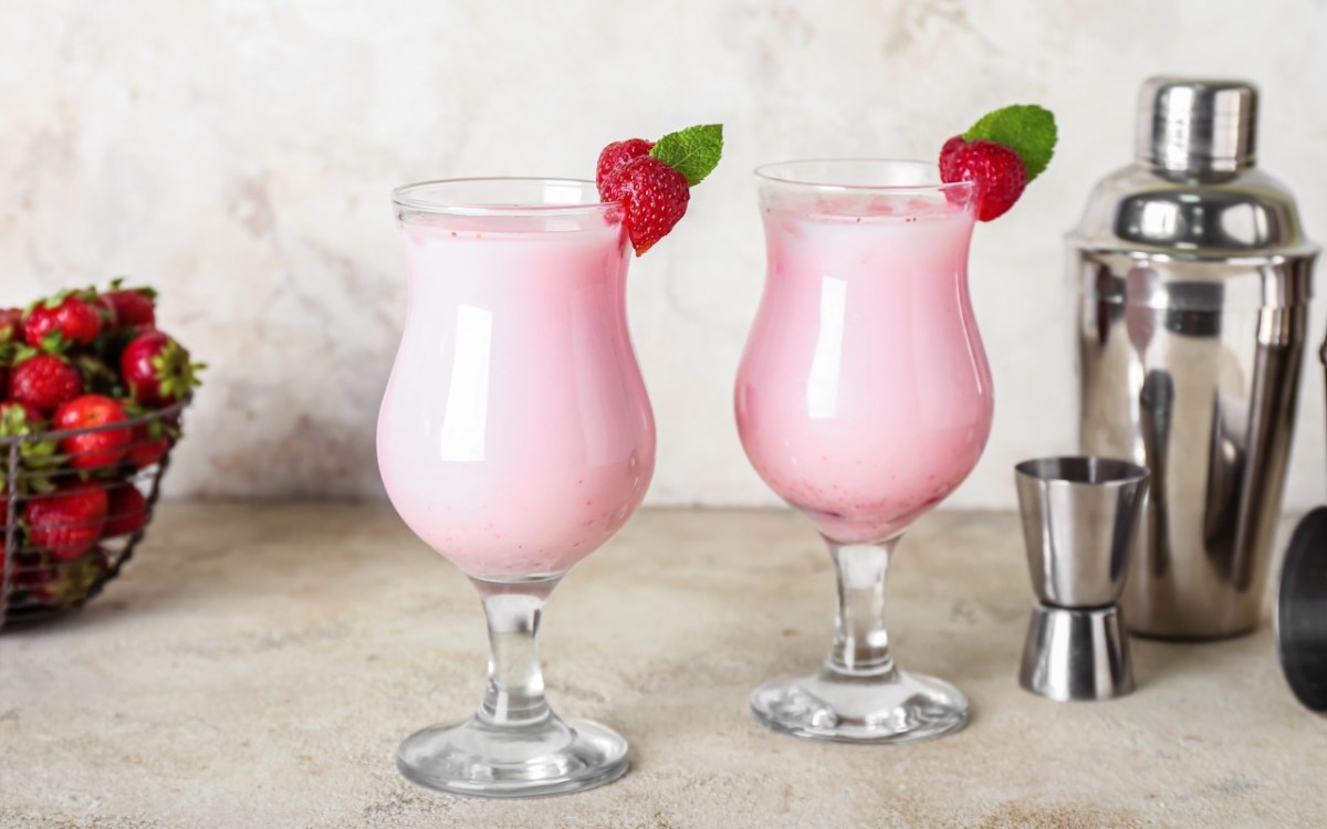Zwei Gläser Strawberry Colada mit Erdbeeren als Deko. Daneben stehen Cocktailshaker.