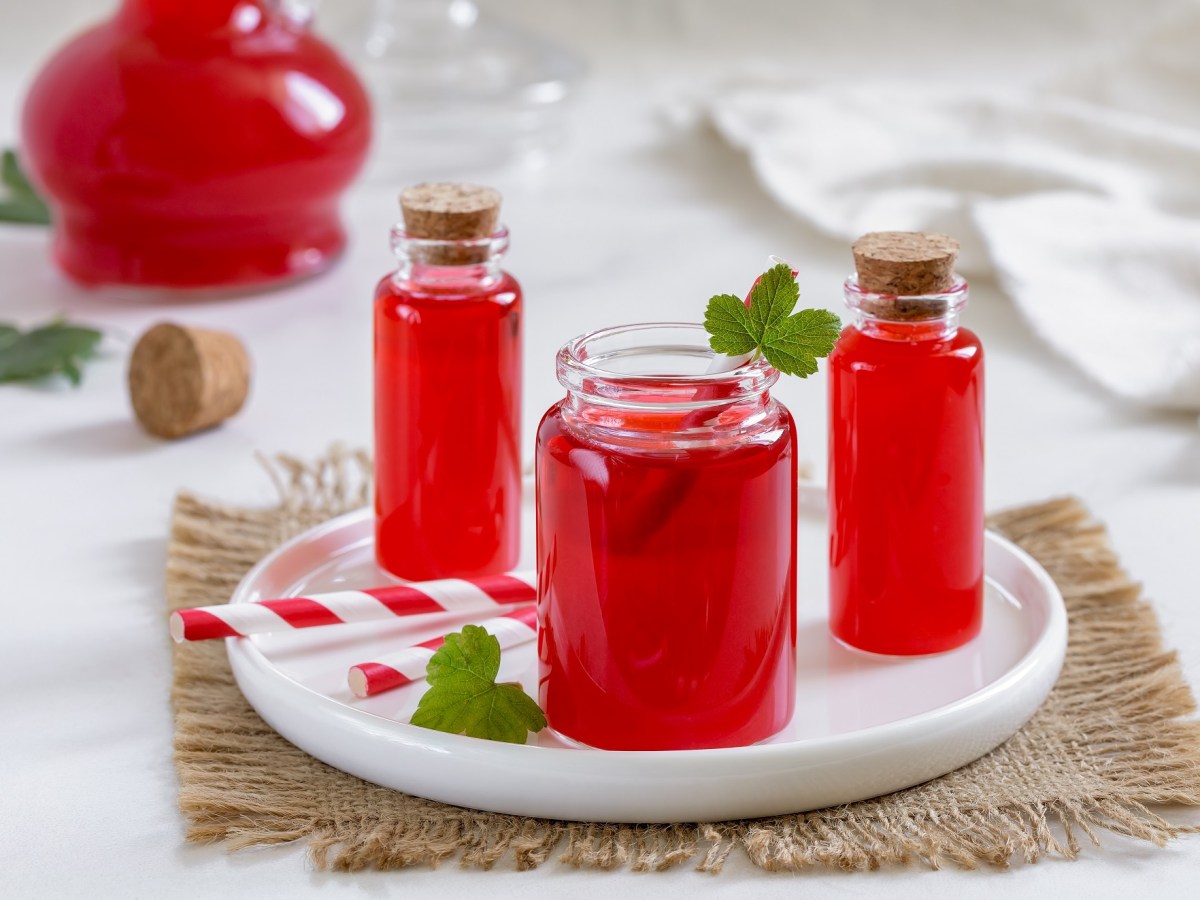 3 Flaschen Wassermelonen-Sirup auf einem weißen Teller, garniert mit Minze, im Hintergrund eine weitere Flasche.