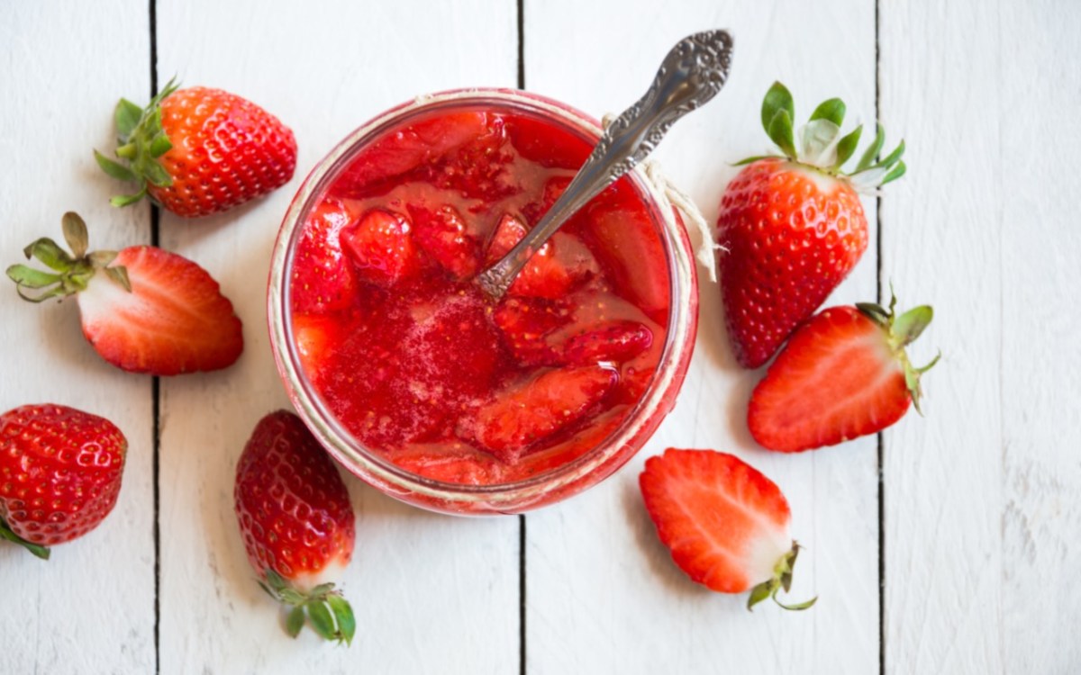 Wie bleibt Erdbeermarmekade rot: Erdbeermarmelade im Glas in der Draufsicht. Daneben frische Erdbeeren.