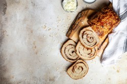 Zimtschnecken-Brot, von dem schon einige Scheiben abgeschnitten sind, auf einem Holzbrett.