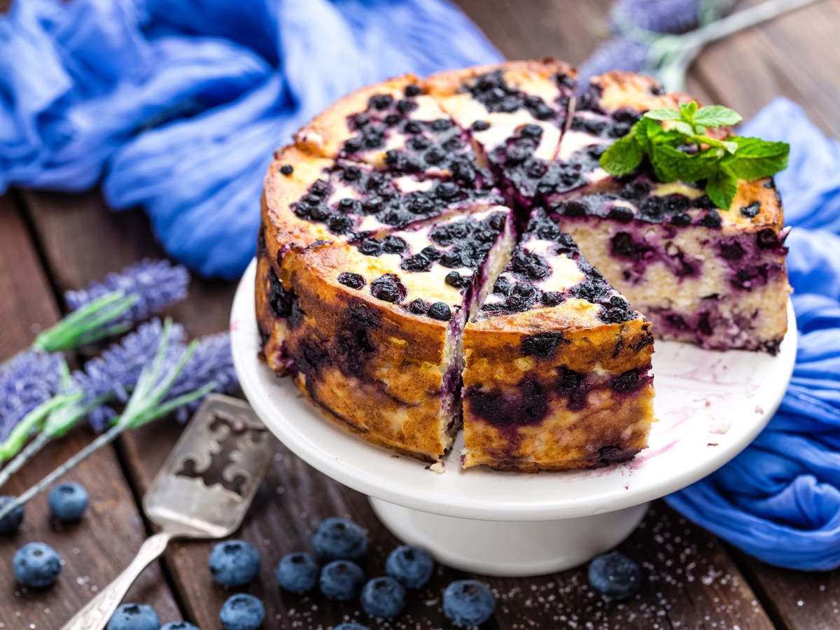 Eine angeschnittene Blaubeer-Joghurt-Torte auf einem dekorierten Tisch.