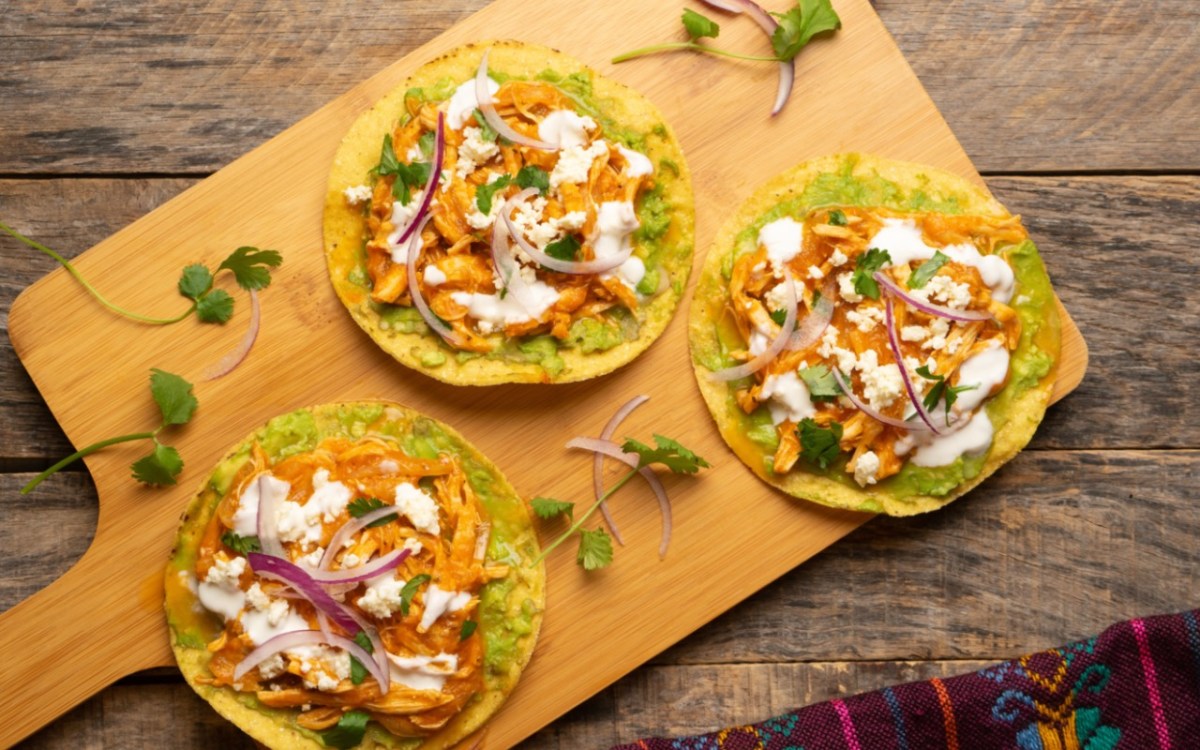 Drei Chicken Tinga Tostadas auf einem Holzbrett in der Draufsicht.