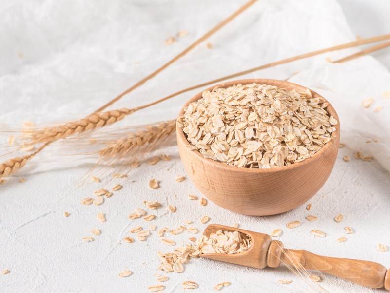 Haferflocken einweichen: eine Schale mit Haferflocken, daneben ein Holzlöffel und Hafer.