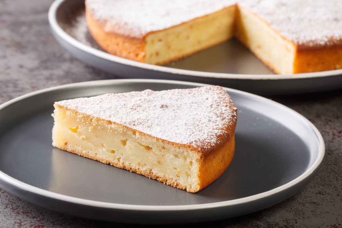 Ein Stück Joghurtkuchen mit 3 Zutaten auf einem Teller. Im Hintergrund der restliche Kuchen.