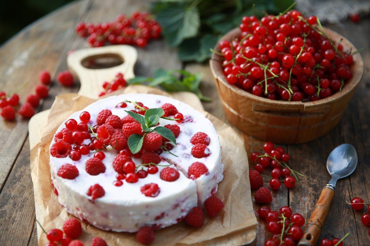 Eine Johannisbeer-Frischkäse-Torte auf einem Tisch voller Beeren.