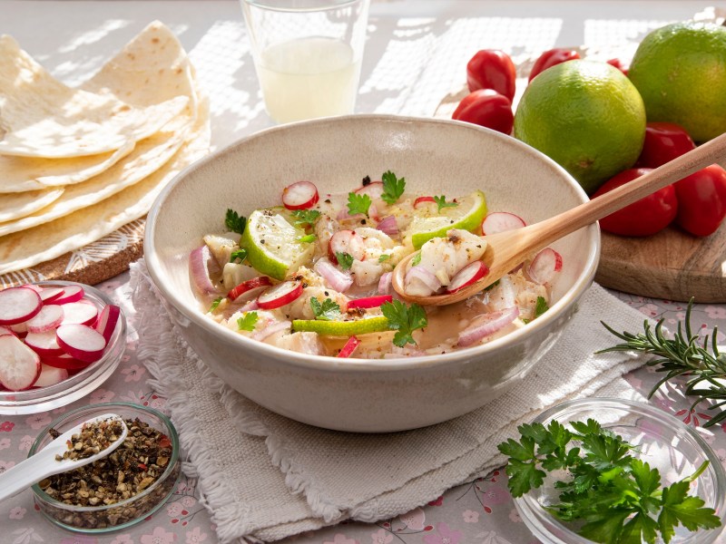 Peruanische Ceviche in einer hellen Schale. Drum herum liegen Limetten, Chilis und Maisfladen.