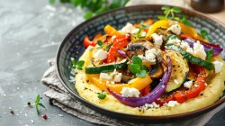 Polenta mit Röstgemüse und Feta in schwarzem Teller.