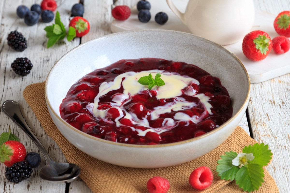 Eine Schüssel Rote Grütze mit Vanillesoße. Drumherum liegen frische Beeren.