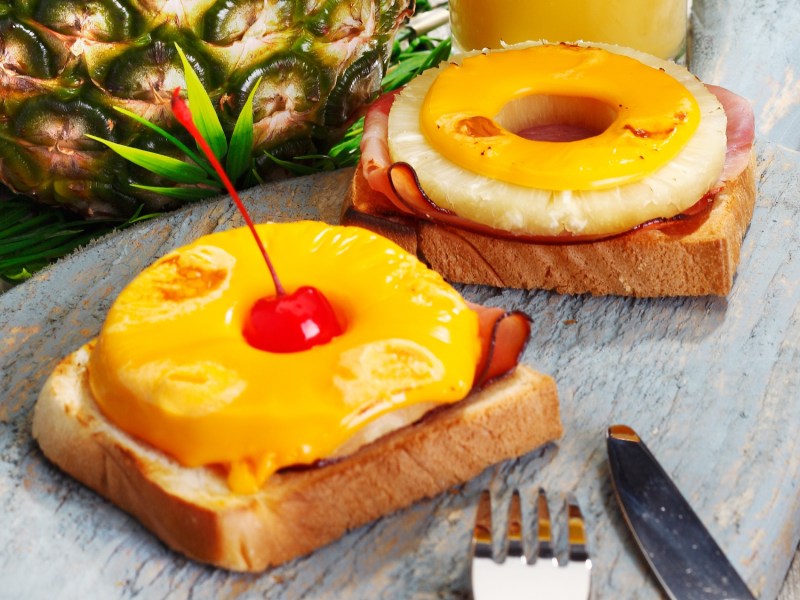 Zwei Stück Toast Hawaii auf einem grauen Marmorteller.