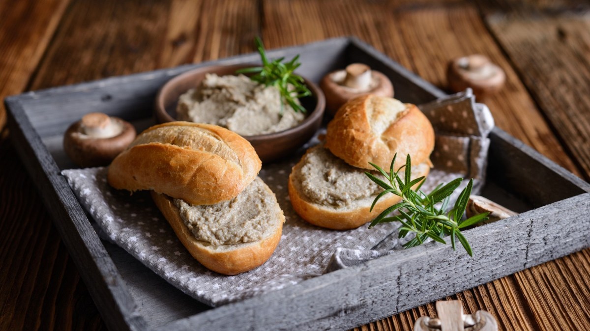 Zwei Brötchen mit Brotaufstrich mit Champignons und Frischkäse auf einem Tablett, daneben Pilze.