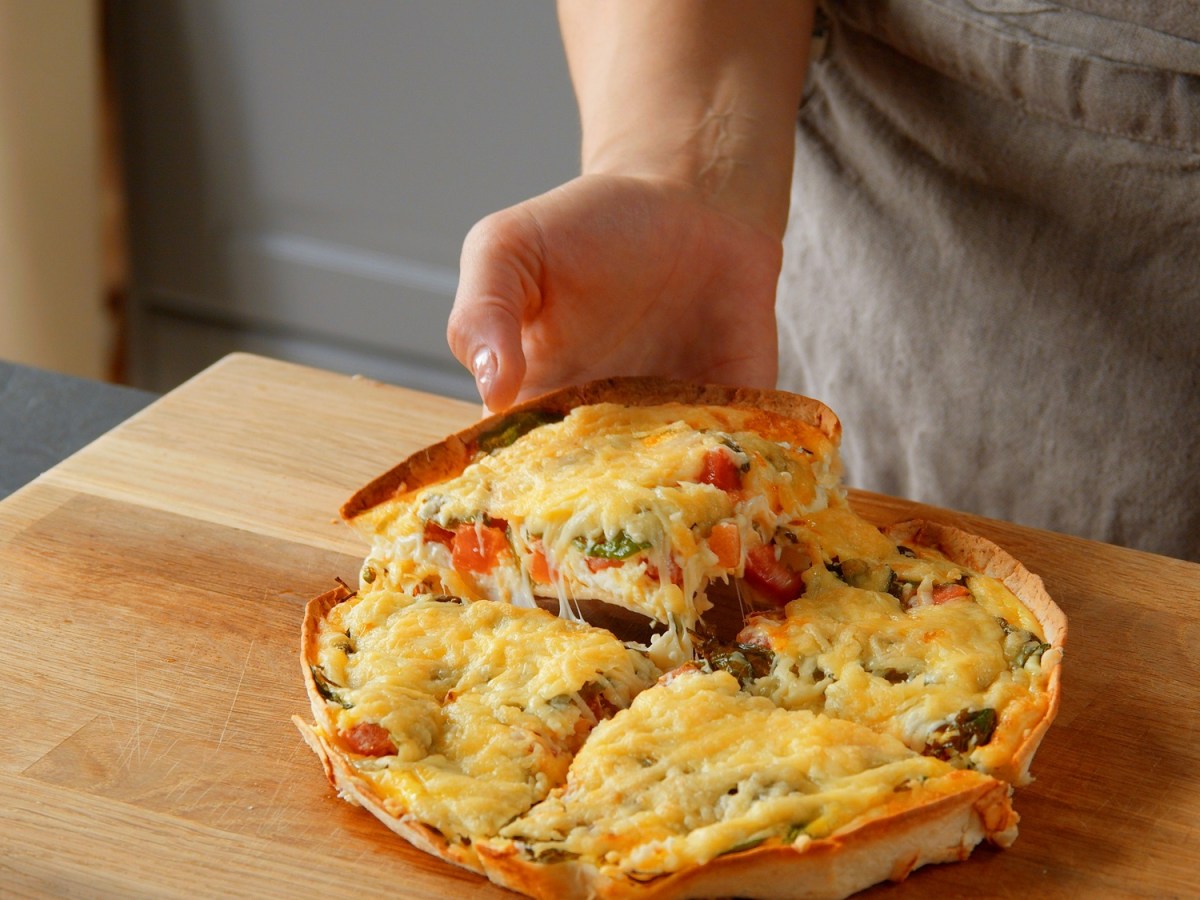 Wrap-Pizza mit Hüttenkäse, in vier Teile geschnitten, ein Stück wird in die Hand genommen.