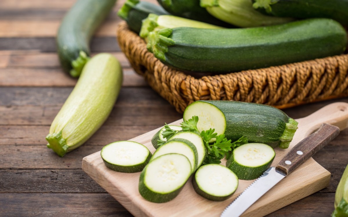 Aufgeschnittene Zucchini auf einem Brett. Im Hintergrund Zucchini in einem Korb.