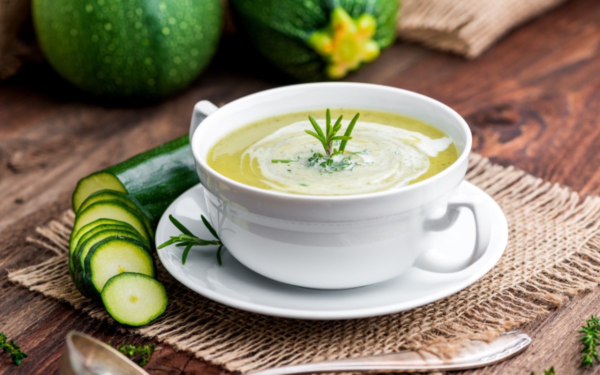 Eine Schüssel mit Zucchini-Suppe. Daneben liegt eine aufgeschnittene Zucchini.