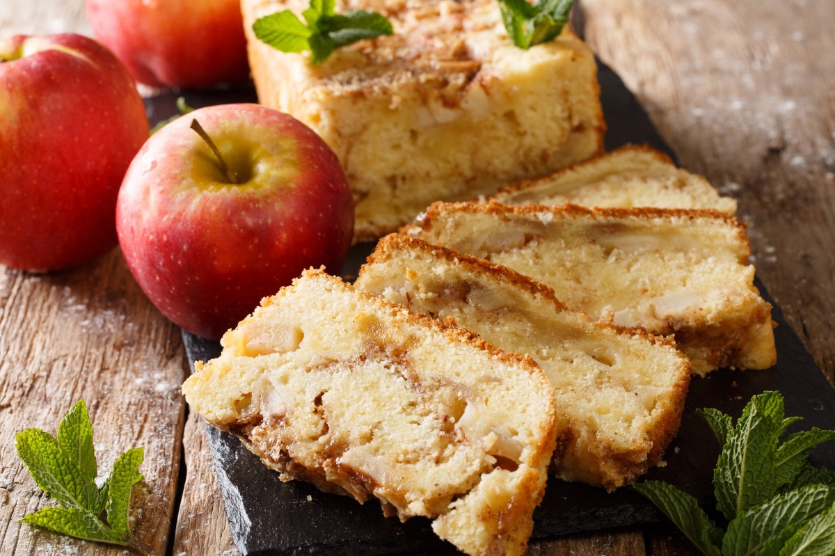 angeschnittener Apfelkuchen aus der Kastenform, daneben ganze Ã„pfel.