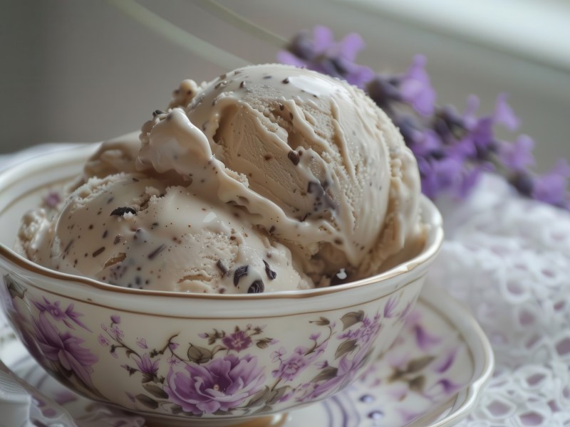 Earl-Grey-Eis in einer fein bemalten Teetasse. Im Hintergrund liegen Lavendelzweige.