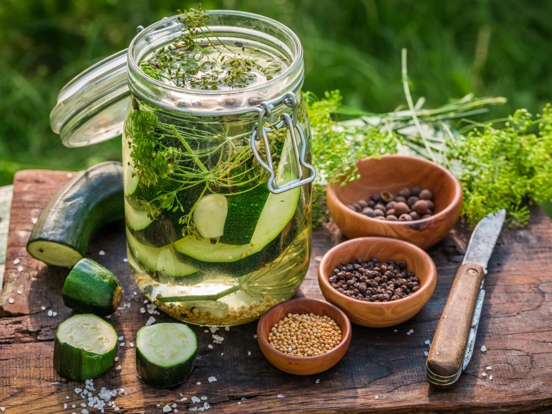 Ein Glas eingelegte Zucchini mit Gewürzen und Messer