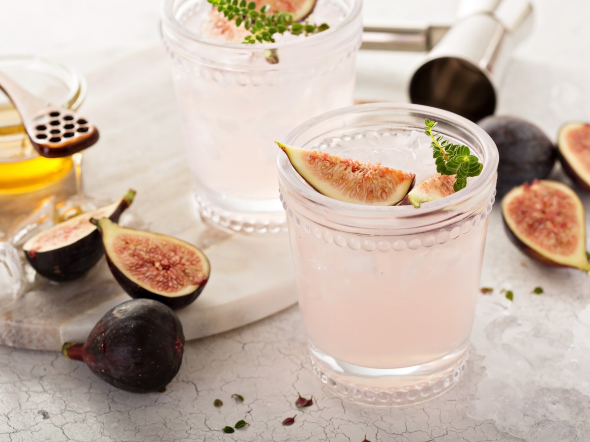 Ein Glas Feigen-Fizz garniert mit einem Stück Feige und Thymian, drumherum Zutaten wie frische Feigen.