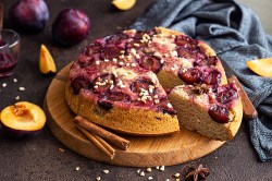 Gestürzter Pflaumenkuchen auf einem Holzbrett. Ein Stück wurde bereits abgeschnitten.