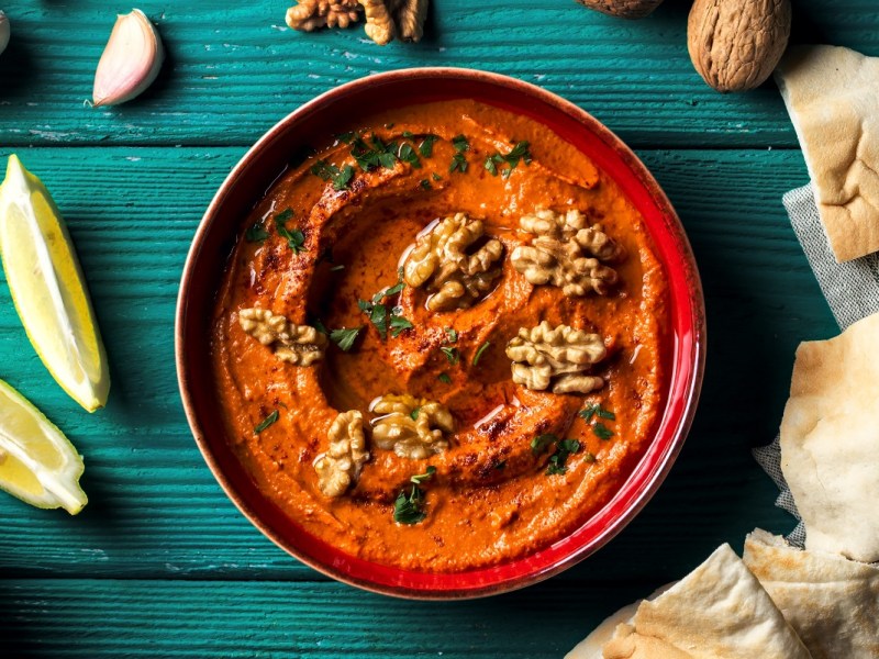 Schale Granatapfel-Paprika-Dip mit Fladenbrot Zitrone und GewÃ¼rze daneben.