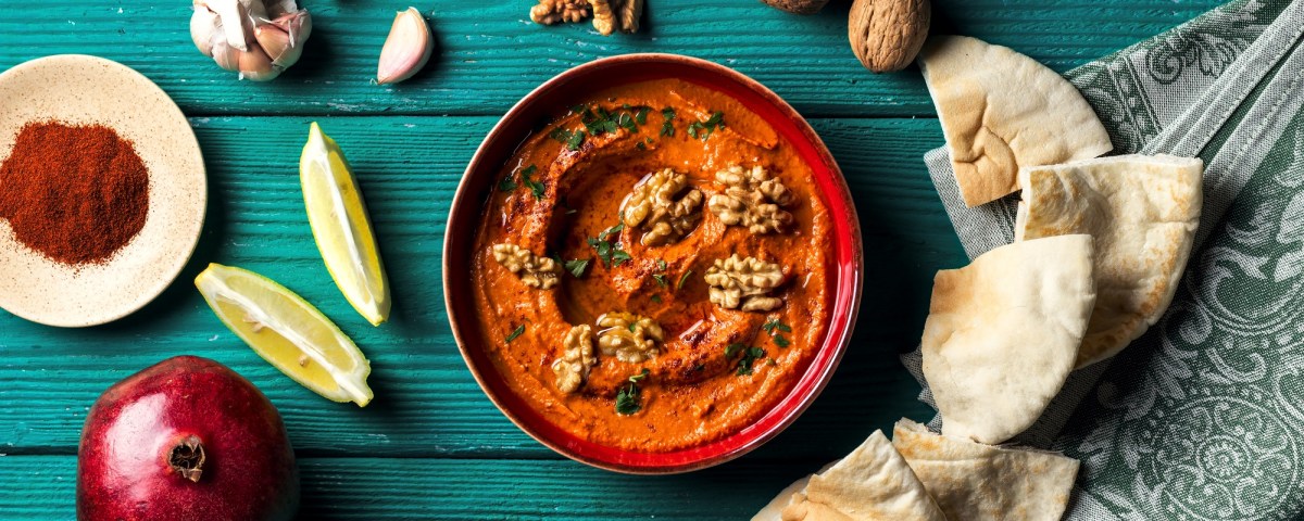 Schale Granatapfel-Paprika-Dip mit Fladenbrot Zitrone und GewÃ¼rze daneben.