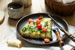 Ein Teller mit einem Stück Mangold-Feta-Frittata garniert mit Tomaten, daneben Messer und Gabel.