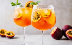 Zwei Gläser Maracuja Spritz mit Orangen- und Maracujascheiben.