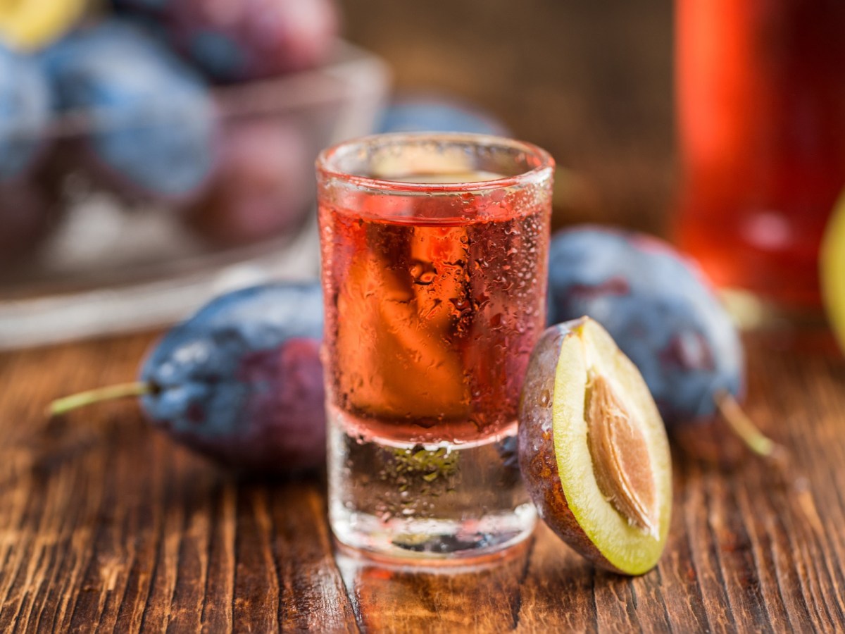 Pflaumen-Gin in einem Glas. Daneben sind frische Pflaumen.