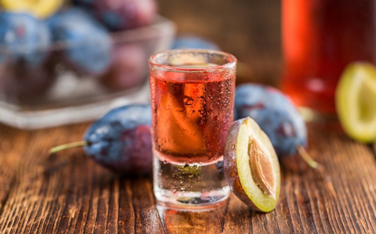 Pflaumen-Gin in einem Glas. Daneben sind frische Pflaumen.