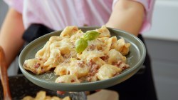 Tortellini in Sahnesoße auf einem grauen Teller.