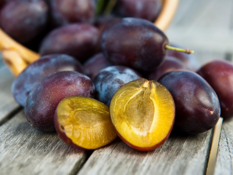 Wie gesund sind Pflaumen: Eine halbierte und mehrere ganze Pflaumen wurden aus einem Korb ausgekippt.