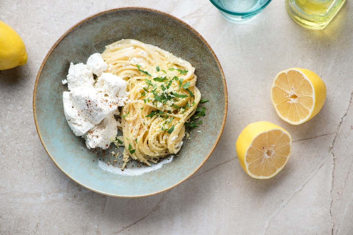 Eine Portion Zitronen-Ricotta-Pasta auf einem blauen Teller. Daneben liegt eine aufgeschnittene Zitrone.