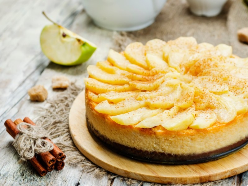 Ein Apfel-Karamell-Käsekuchen. Daneben liegen Zimtstangen.