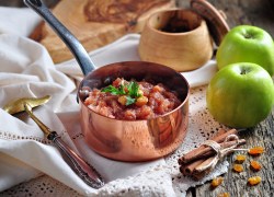 Ein kleiner Topf mit Apfelchutney und Rosinen, drumherum frische grüne Äpfel, Sultaninen und Zubehör.