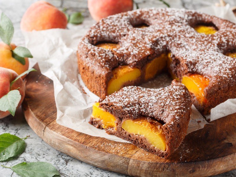 Ein angeschnittener Aprikosen-Schokoladenkuchen auf einem Holzbrett.