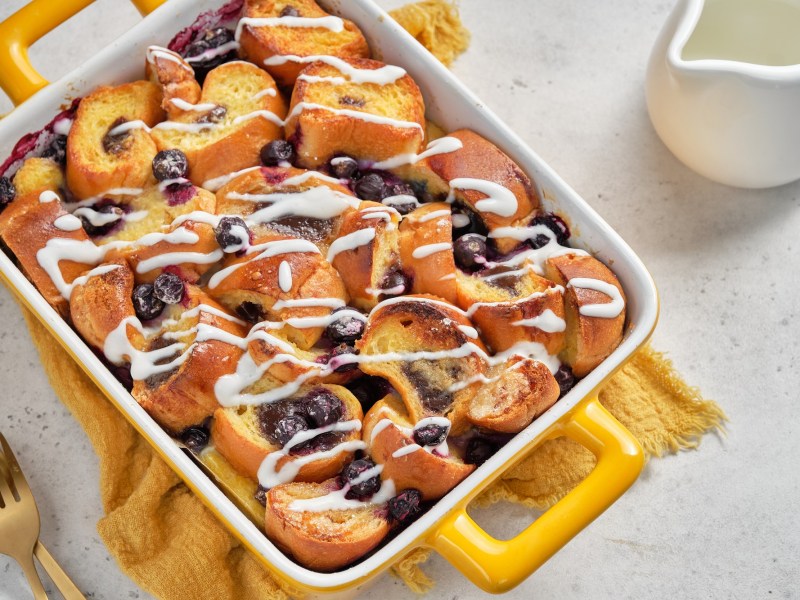 Brotauflauf mit Blaubeeren und Frosting in gelber Auflaufform.