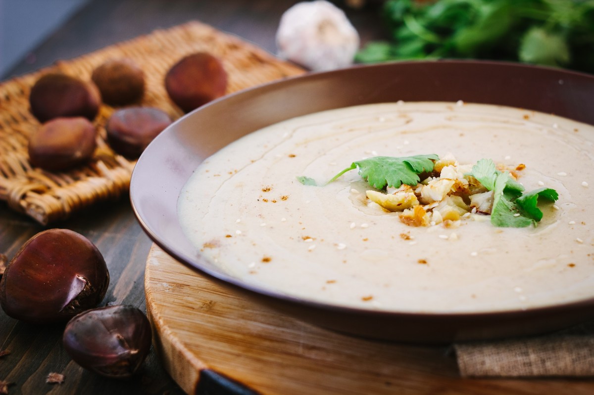 Ein Teller franzÃ¶sische Maronensuppe garniert mit Maronen und KrÃ¤utern, drumherum Esskastanien.