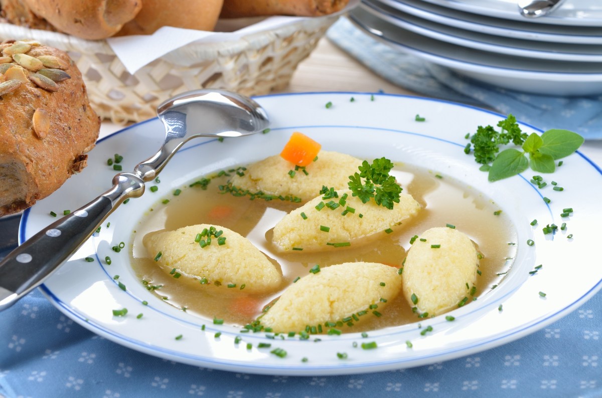 GrieÃŸschÃ¶berl-Suppe auf einem Teller, daneben ein BrÃ¶tchen. Nahaufnahme.