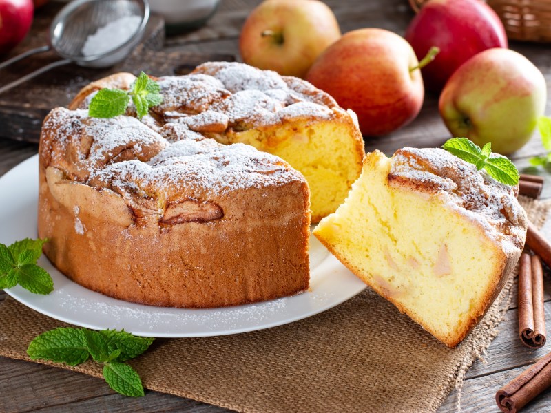 Angeschnittener italienischer Apfelkuchen Torta di Mele auf einem Teller. Drumherum Äpfel.