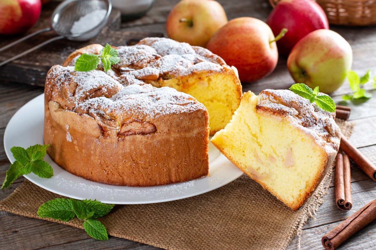 Angeschnittener italienischer Apfelkuchen Torta di Mele auf einem Teller. Drumherum Ã„pfel.