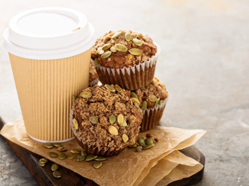 Kaffeemuffins mit KÃ¼rbiskernen neben einem Pappbecher Kaffee.