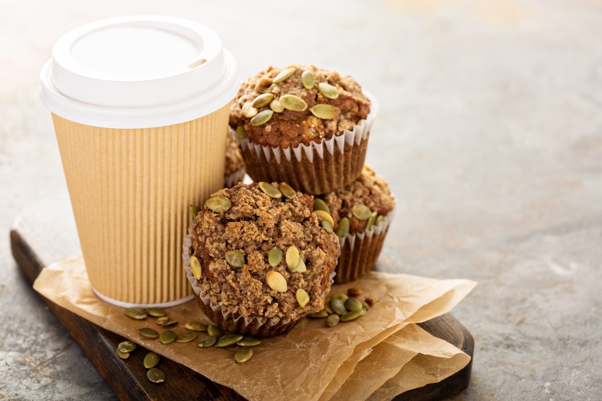 Kaffeemuffins mit KÃ¼rbiskernen neben einem Pappbecher Kaffee.