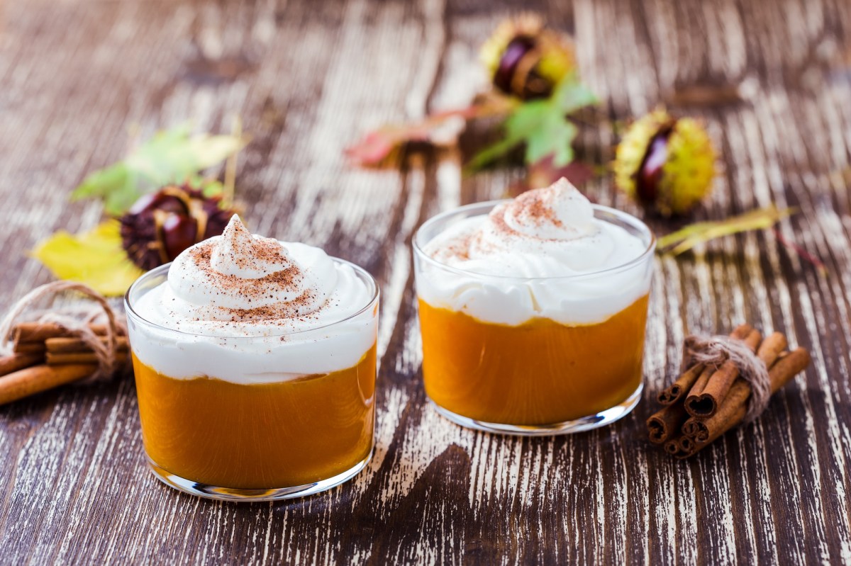 zwei GlÃ¤ser KÃ¼rbis-Mousse mit Sahnehaube und Zimt bestreut, drumherum Kastanien.