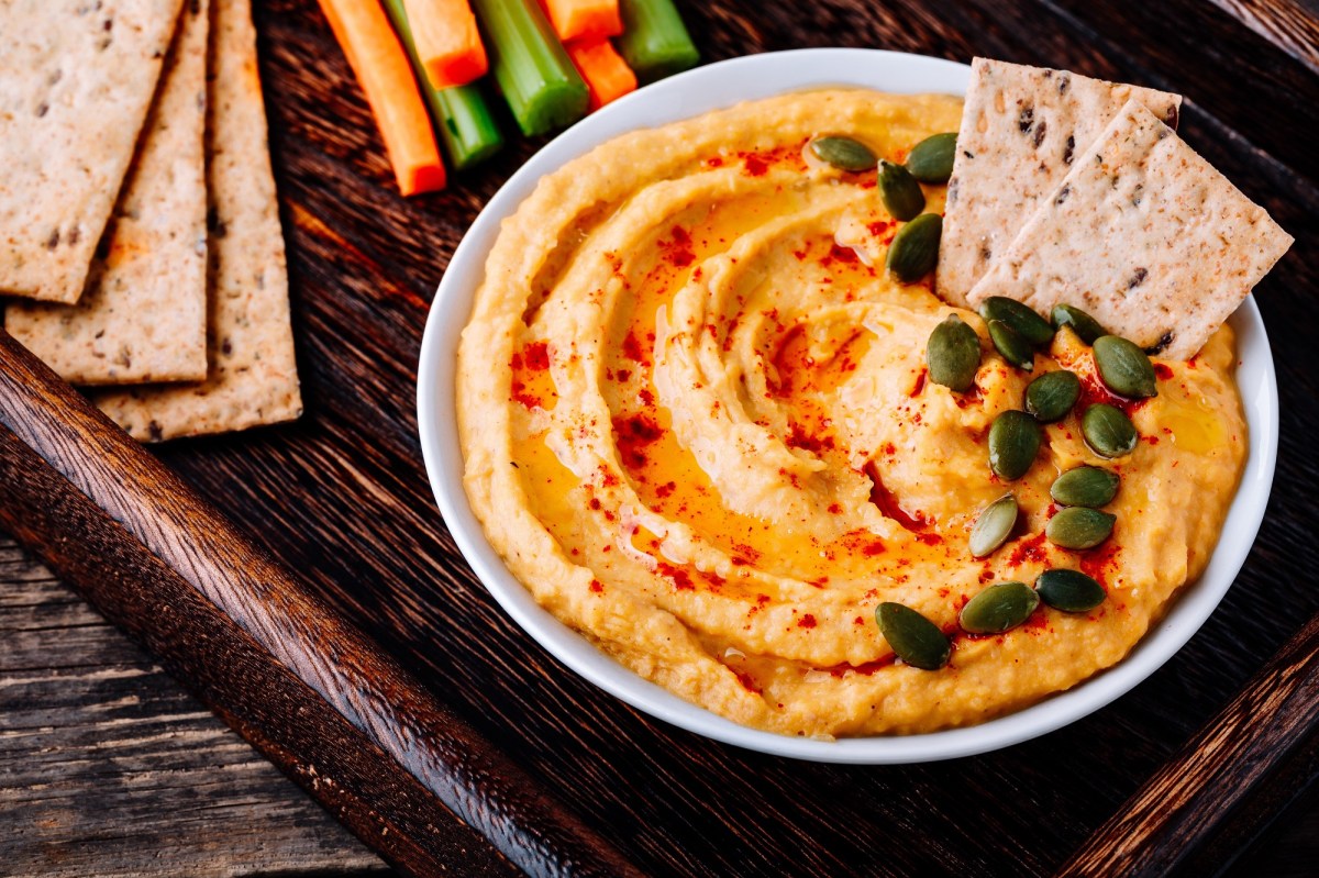 Schale mit KÃ¼rbis-FrischkÃ¤se-Dip auf Tablett, Cracker und GemÃ¼sesticks