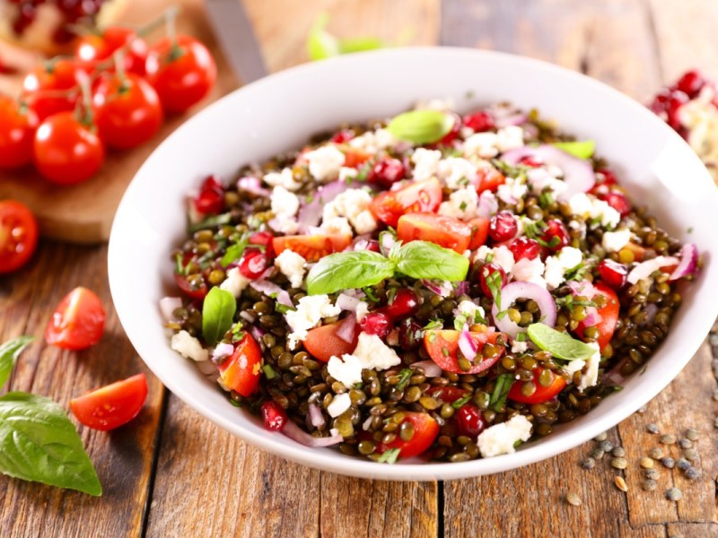 Eine Schüssel Linsensalat mit Feta. Daneben liegen frische Zutaten.