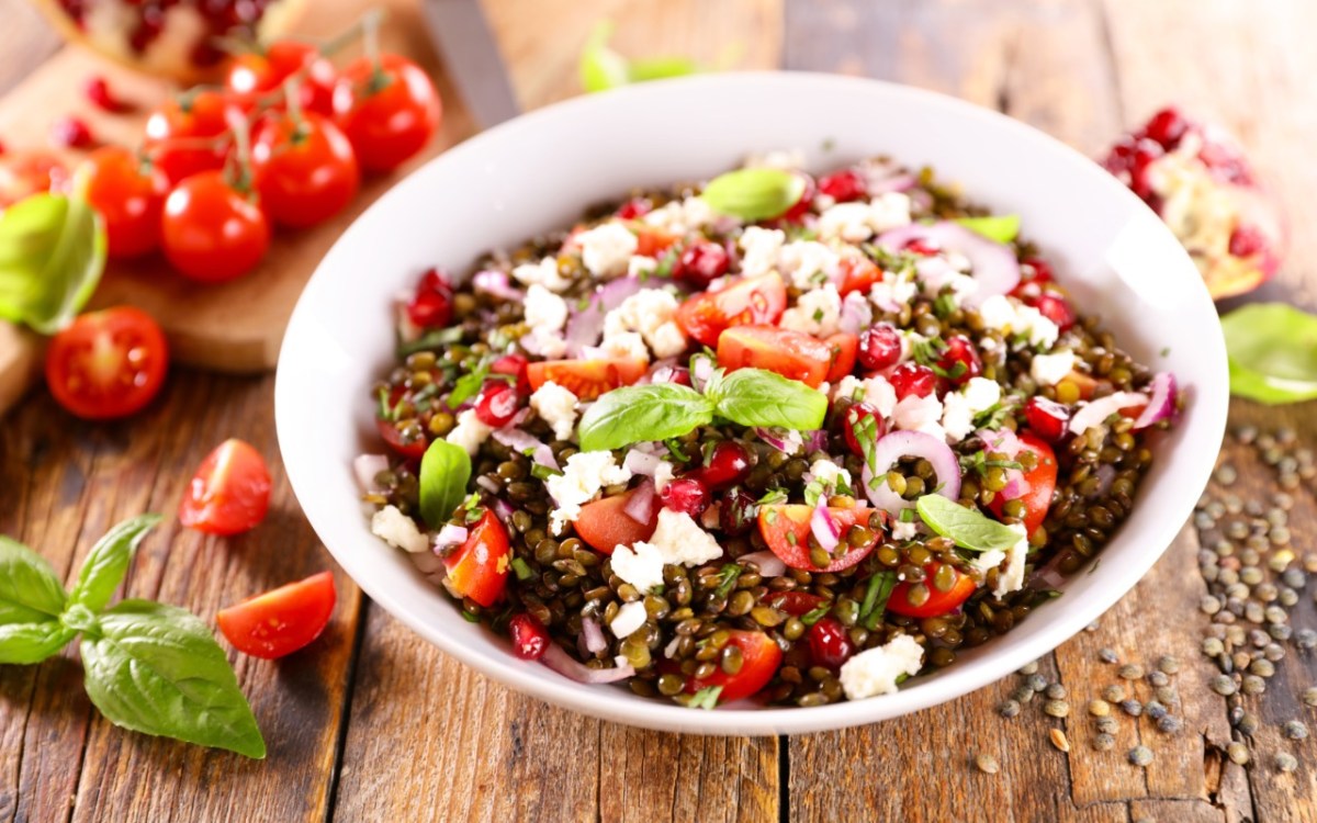 Eine SchÃ¼ssel Linsensalat mit Feta. Daneben liegen frische Zutaten.